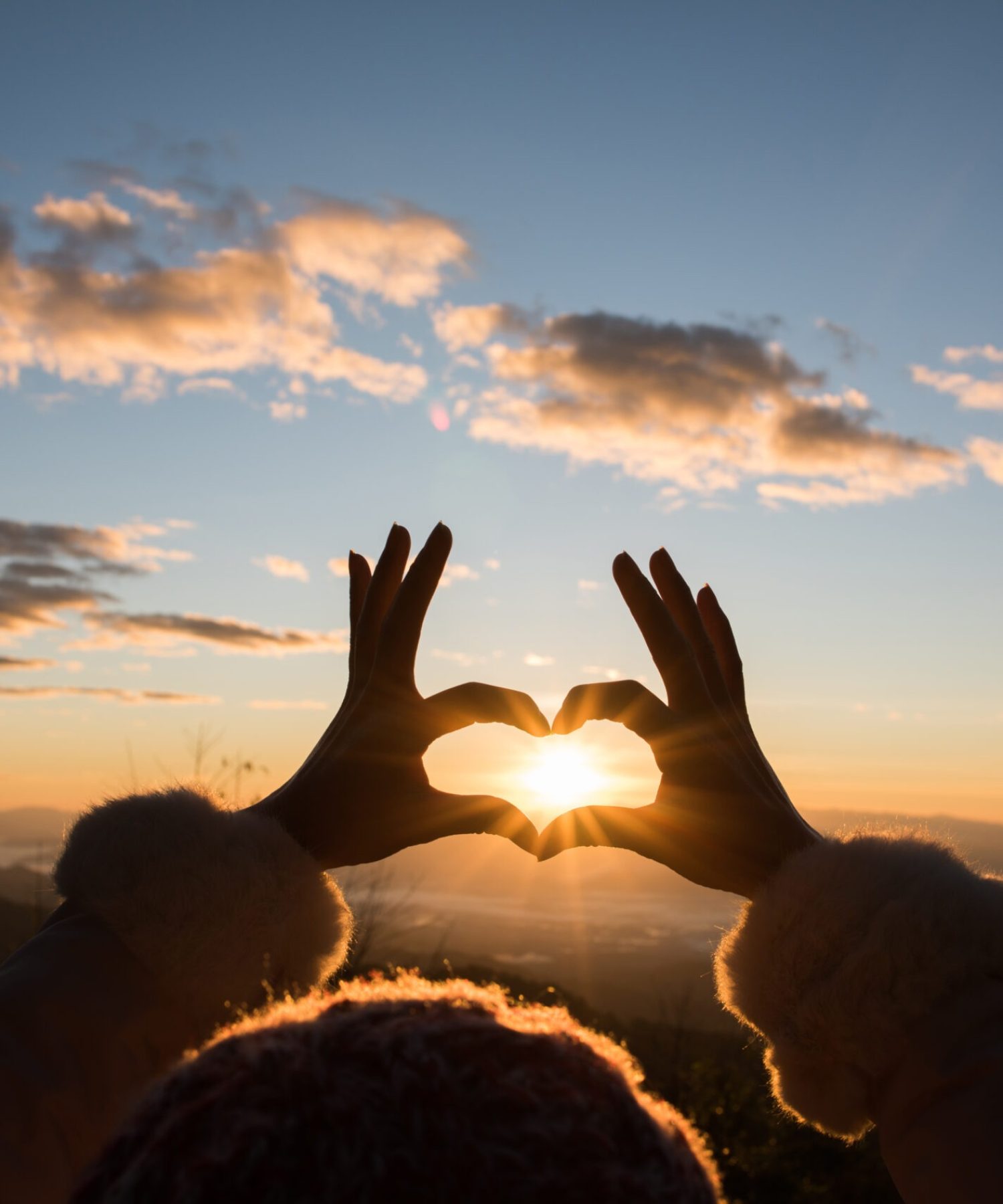Silhouette hands forming a heart shape with sunrise